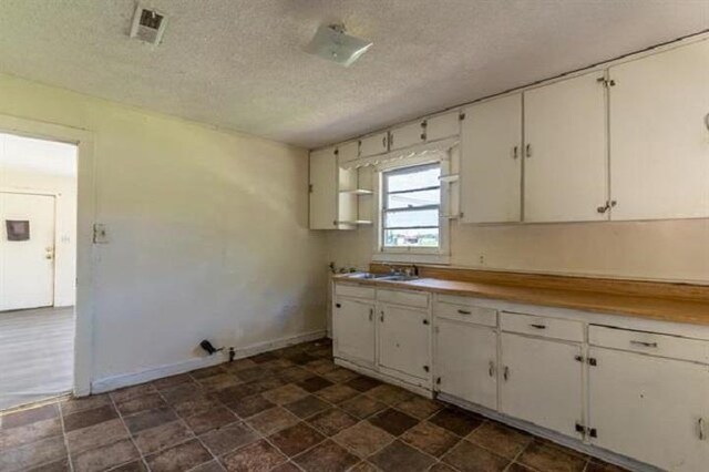 kitchen featuring a textured ceiling, white cabinetry, and sink