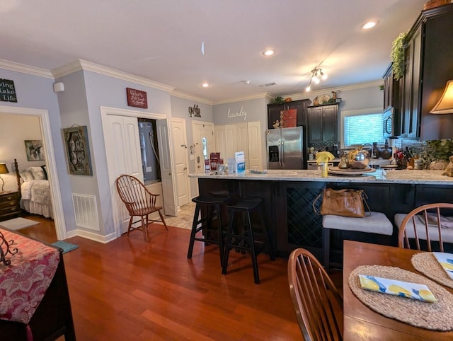 kitchen with kitchen peninsula, stainless steel appliances, dark wood-type flooring, crown molding, and a breakfast bar