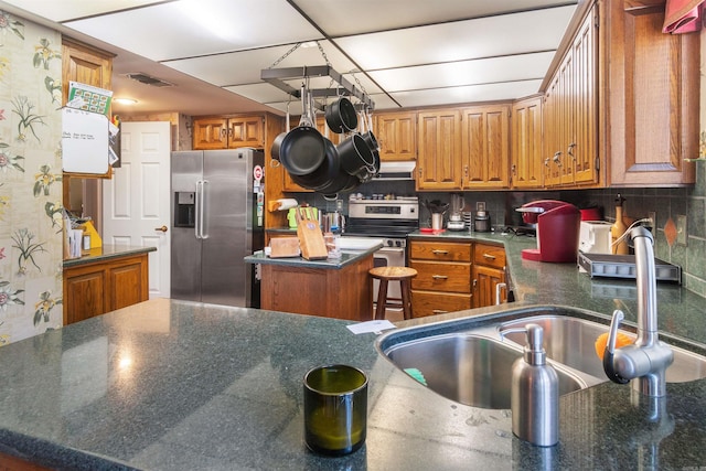 kitchen with stainless steel appliances, decorative backsplash, a center island, dark stone counters, and sink