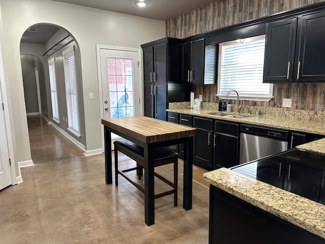 kitchen featuring stainless steel dishwasher, light stone countertops, sink, and wooden walls