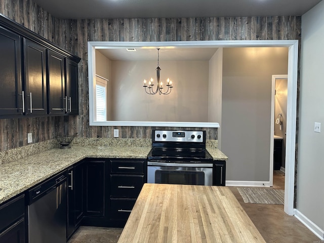 kitchen featuring wood walls, stainless steel appliances, decorative light fixtures, a notable chandelier, and light stone counters