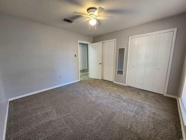 unfurnished bedroom featuring ceiling fan, a textured ceiling, carpet, and two closets