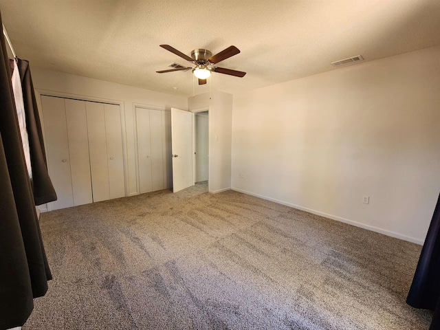 unfurnished bedroom featuring ceiling fan, carpet floors, and two closets