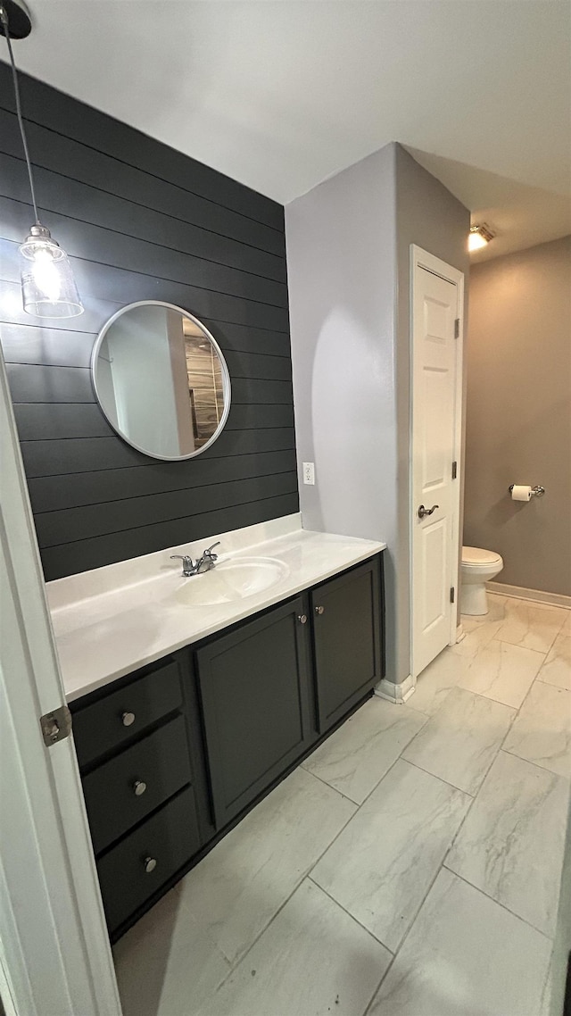 bathroom with toilet, vanity, and wood walls