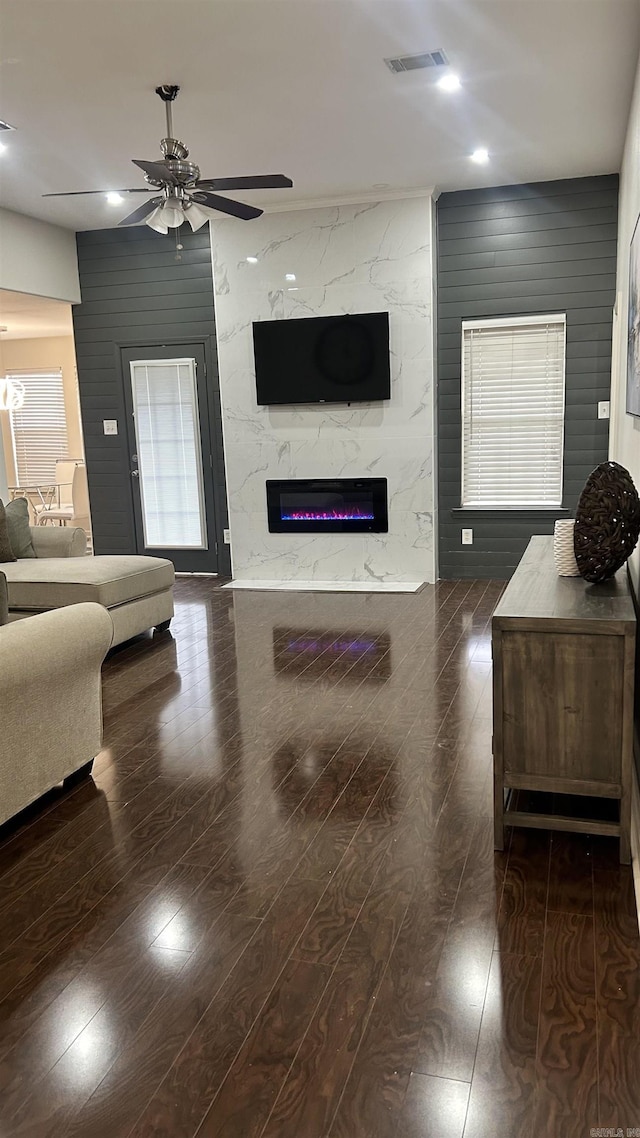 living room with ceiling fan, dark wood-type flooring, a premium fireplace, and wood walls