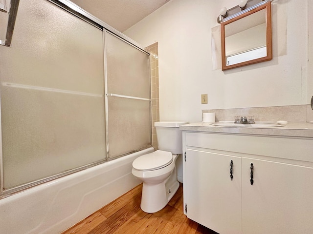 full bathroom featuring wood-type flooring, shower / bath combination with glass door, vanity, and toilet