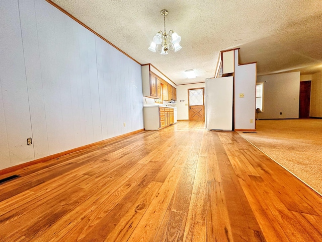 unfurnished living room featuring crown molding, wood walls, an inviting chandelier, and light hardwood / wood-style floors