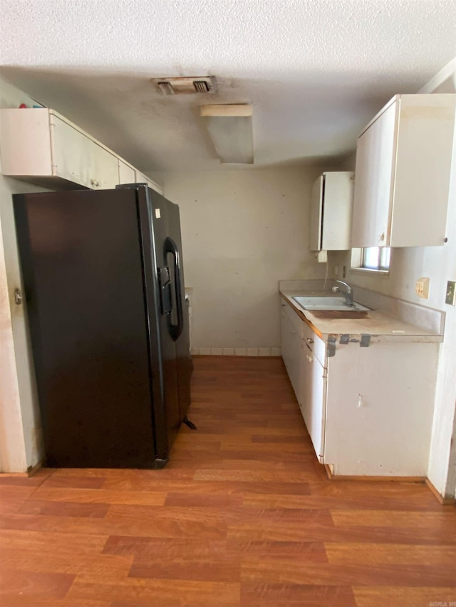 kitchen with light hardwood / wood-style floors, black fridge, sink, white cabinetry, and a textured ceiling