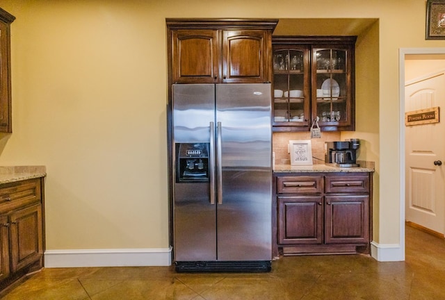 kitchen with stainless steel refrigerator with ice dispenser, light stone countertops, dark tile patterned flooring, and dark brown cabinets