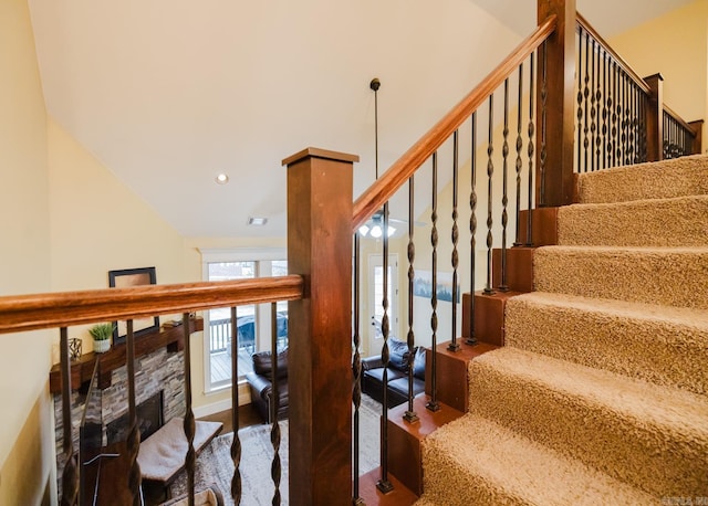 staircase featuring lofted ceiling and a stone fireplace