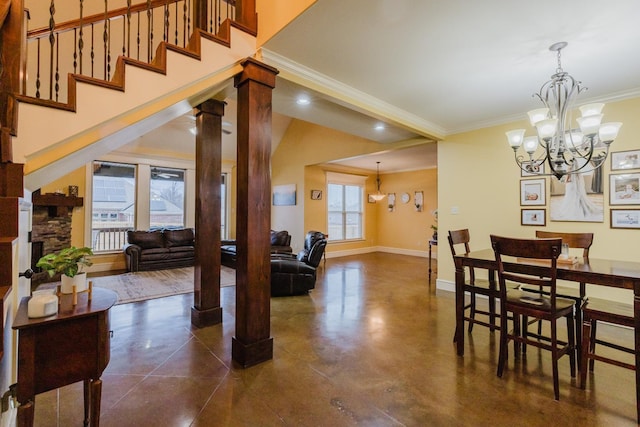 dining space with decorative columns, crown molding, a stone fireplace, and a notable chandelier