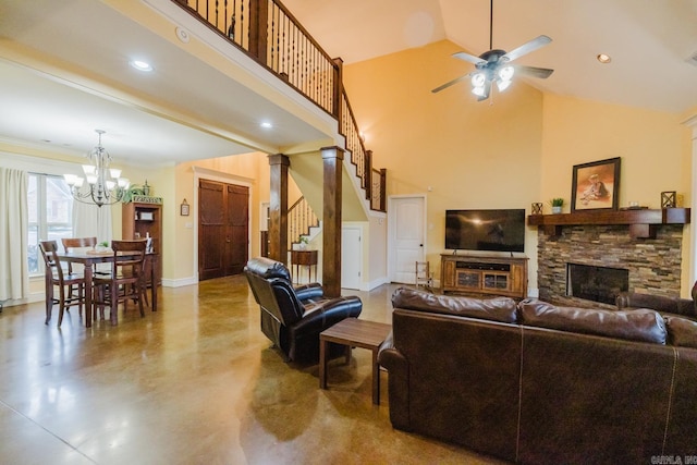 living room with ceiling fan with notable chandelier, a towering ceiling, ornate columns, a stone fireplace, and concrete floors