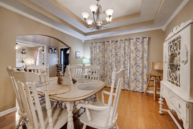 dining area with ornamental molding, light hardwood / wood-style floors, a tray ceiling, and a notable chandelier