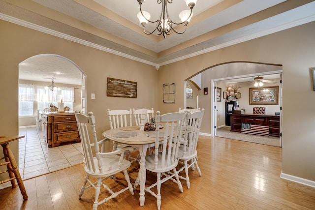 dining room featuring ceiling fan with notable chandelier, a tray ceiling, crown molding, and light wood-type flooring