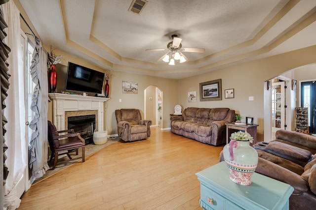 living room featuring ceiling fan, light hardwood / wood-style floors, a textured ceiling, and a tray ceiling