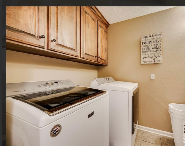 laundry area featuring washer and clothes dryer, light tile patterned floors, a textured ceiling, and cabinets