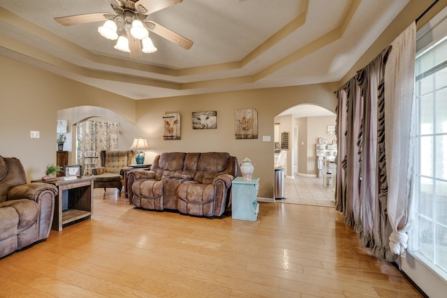 living room featuring ceiling fan, light hardwood / wood-style floors, and a tray ceiling