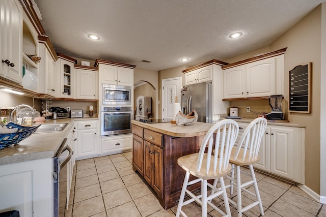 kitchen with light tile patterned floors, stainless steel appliances, a kitchen island, a breakfast bar, and sink