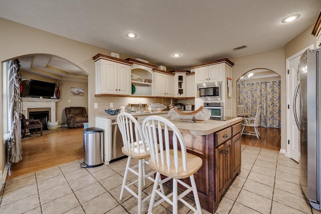 kitchen featuring a kitchen island, appliances with stainless steel finishes, a kitchen breakfast bar, a textured ceiling, and light tile patterned floors