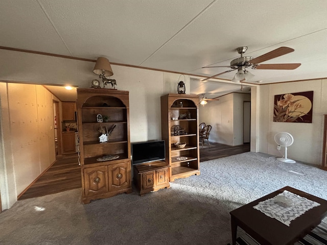 living room featuring a textured ceiling, ceiling fan, ornamental molding, and dark carpet