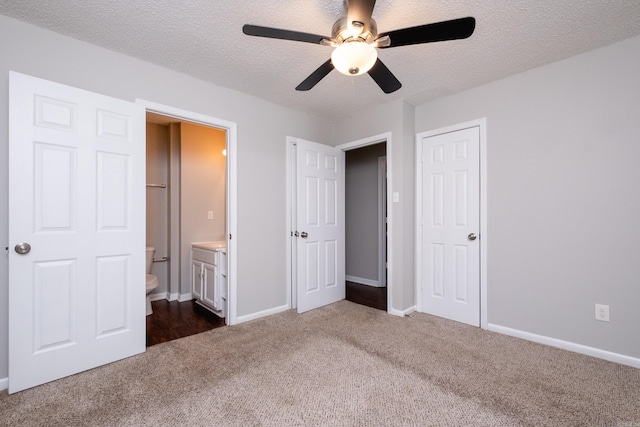 unfurnished bedroom featuring ensuite bath, ceiling fan, a textured ceiling, and dark colored carpet