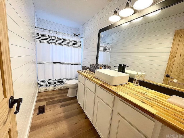 bathroom with toilet, vanity, wood walls, wood-type flooring, and curtained shower