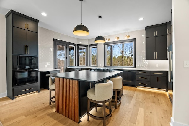 kitchen with a center island, black appliances, hanging light fixtures, light wood-type flooring, and a breakfast bar area