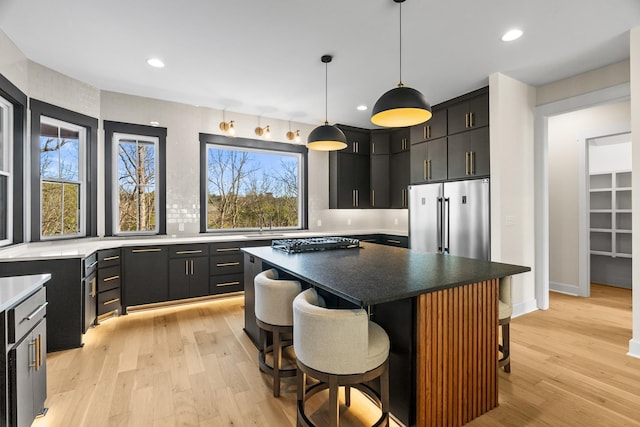 kitchen featuring high quality fridge, a kitchen island, a kitchen bar, decorative light fixtures, and light wood-type flooring