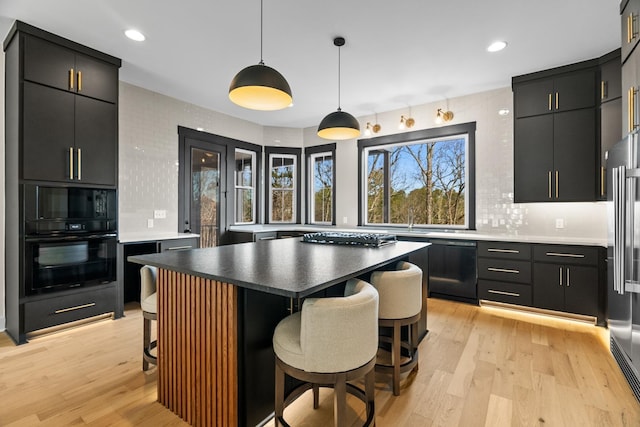 kitchen featuring black appliances, a kitchen island, decorative light fixtures, light hardwood / wood-style floors, and a breakfast bar