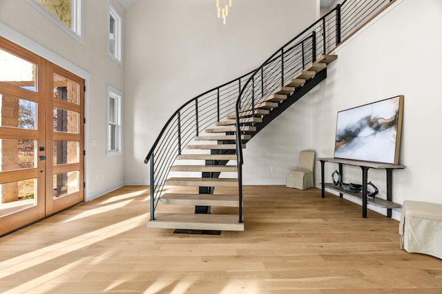 foyer entrance featuring light wood-type flooring, a towering ceiling, and french doors