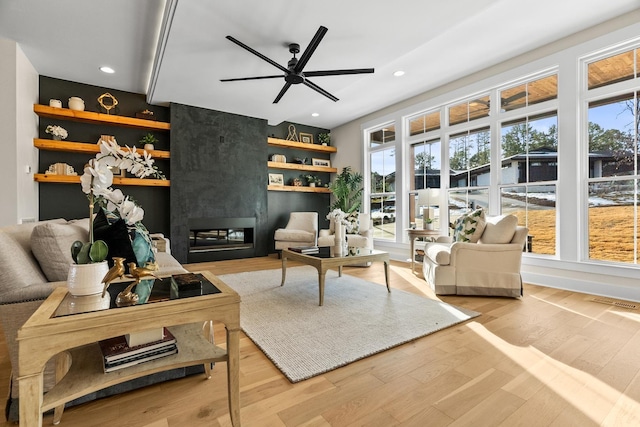 living room with light hardwood / wood-style floors, built in shelves, ceiling fan, and a fireplace