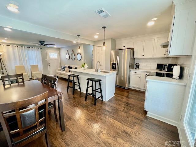 kitchen with ceiling fan, hanging light fixtures, appliances with stainless steel finishes, an island with sink, and white cabinets