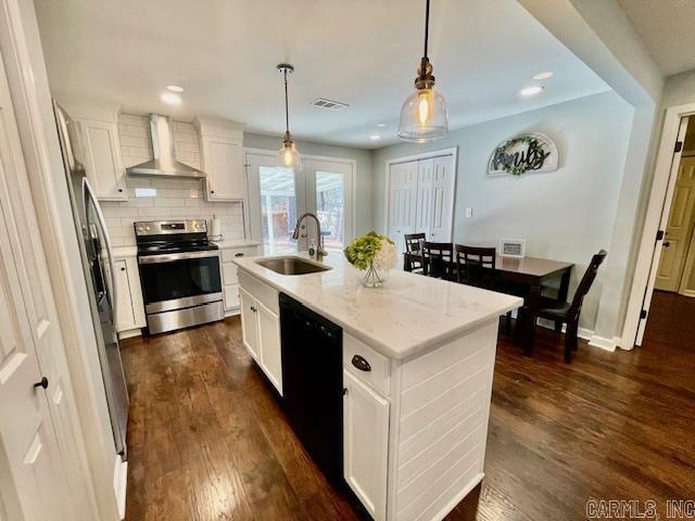 kitchen featuring pendant lighting, white cabinetry, wall chimney range hood, stainless steel appliances, and a center island with sink