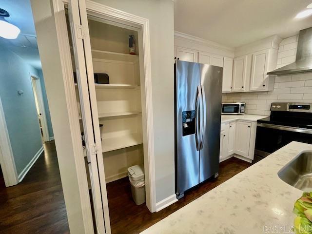 kitchen featuring light stone countertops, white cabinets, appliances with stainless steel finishes, wall chimney exhaust hood, and decorative backsplash