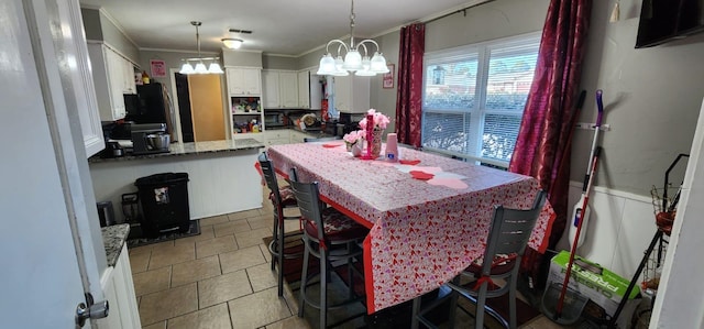 kitchen featuring white cabinets, ornamental molding, a notable chandelier, light tile patterned floors, and a breakfast bar area