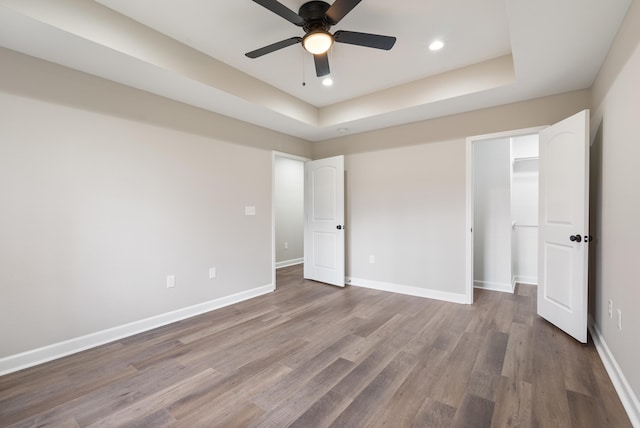 unfurnished bedroom featuring hardwood / wood-style floors, a walk in closet, a closet, ceiling fan, and a tray ceiling