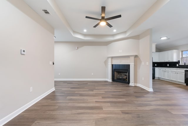 unfurnished living room with ceiling fan, a tray ceiling, light hardwood / wood-style flooring, and a fireplace