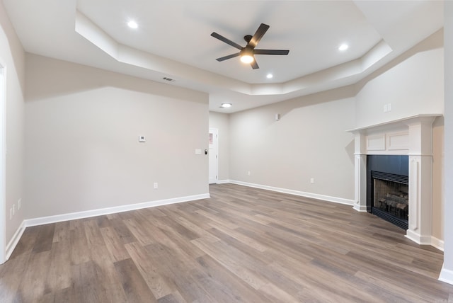 unfurnished living room featuring ceiling fan, wood-type flooring, and a tray ceiling