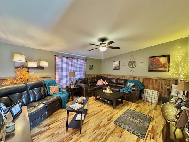 living room featuring ceiling fan, light hardwood / wood-style flooring, lofted ceiling, and wooden walls