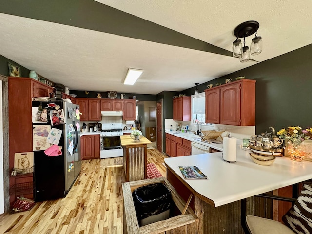 kitchen featuring kitchen peninsula, white appliances, light hardwood / wood-style flooring, a breakfast bar, and sink