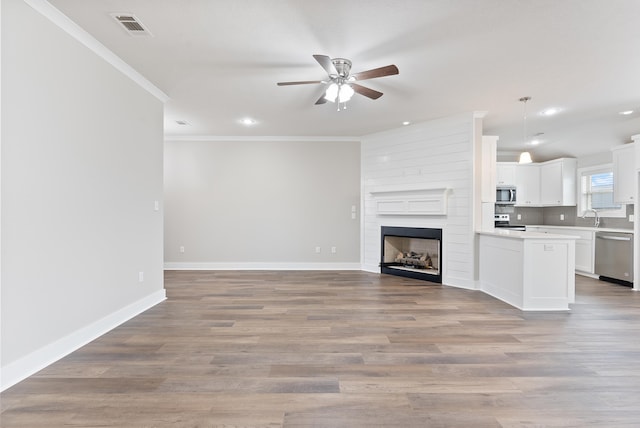 unfurnished living room featuring ceiling fan, a fireplace, sink, crown molding, and light hardwood / wood-style flooring