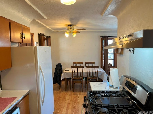 kitchen with white fridge, light hardwood / wood-style floors, stainless steel range with gas stovetop, ceiling fan, and a textured ceiling