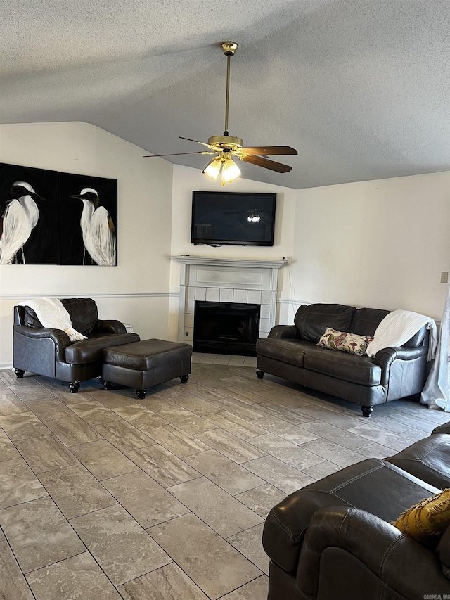 living room featuring ceiling fan, a tiled fireplace, and a textured ceiling