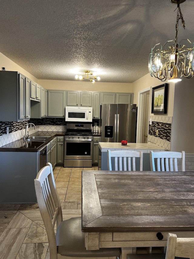 kitchen with a notable chandelier, decorative backsplash, sink, appliances with stainless steel finishes, and a textured ceiling