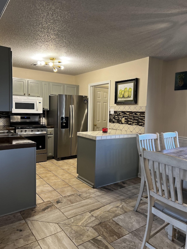 kitchen featuring a textured ceiling, appliances with stainless steel finishes, gray cabinetry, and tile counters