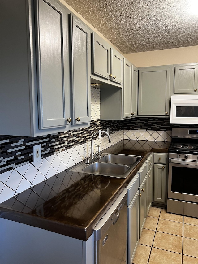 kitchen featuring sink, light tile patterned floors, stainless steel range oven, gray cabinetry, and dishwashing machine