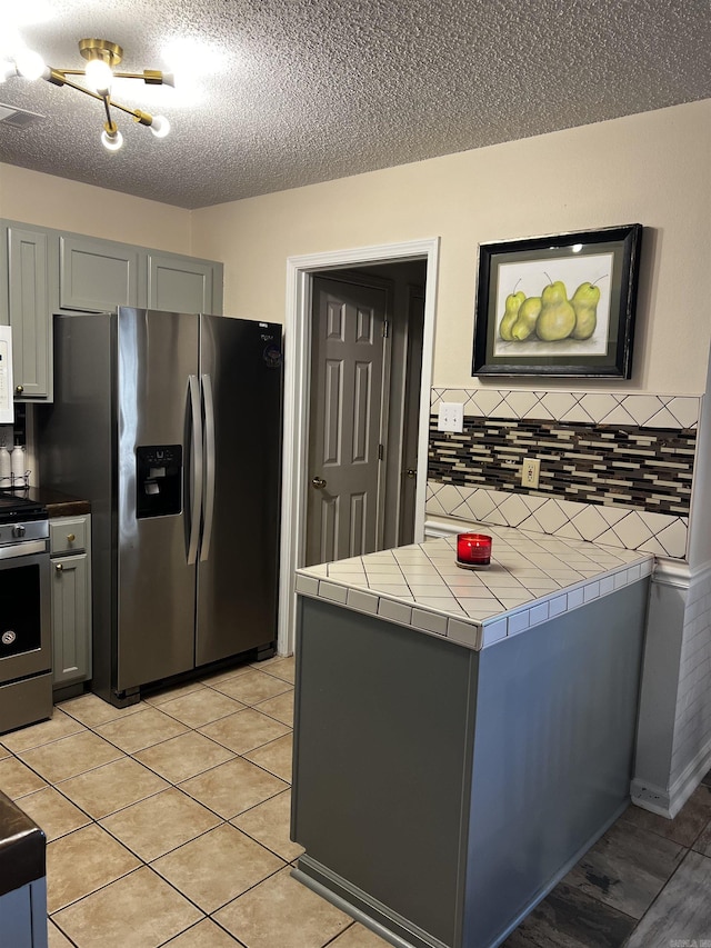 kitchen with gray cabinetry, decorative backsplash, tile countertops, and stainless steel appliances