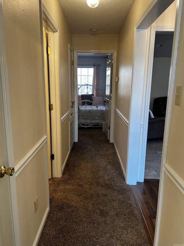 hall with a textured ceiling and dark carpet