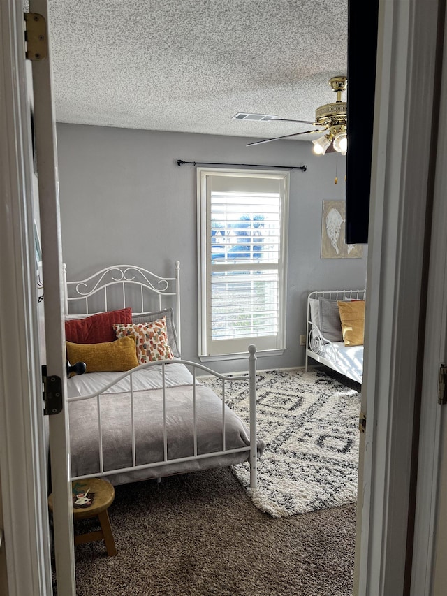 carpeted bedroom featuring ceiling fan and a textured ceiling