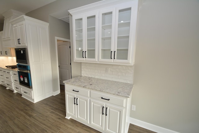 kitchen featuring stainless steel oven, white cabinets, light stone countertops, and tasteful backsplash